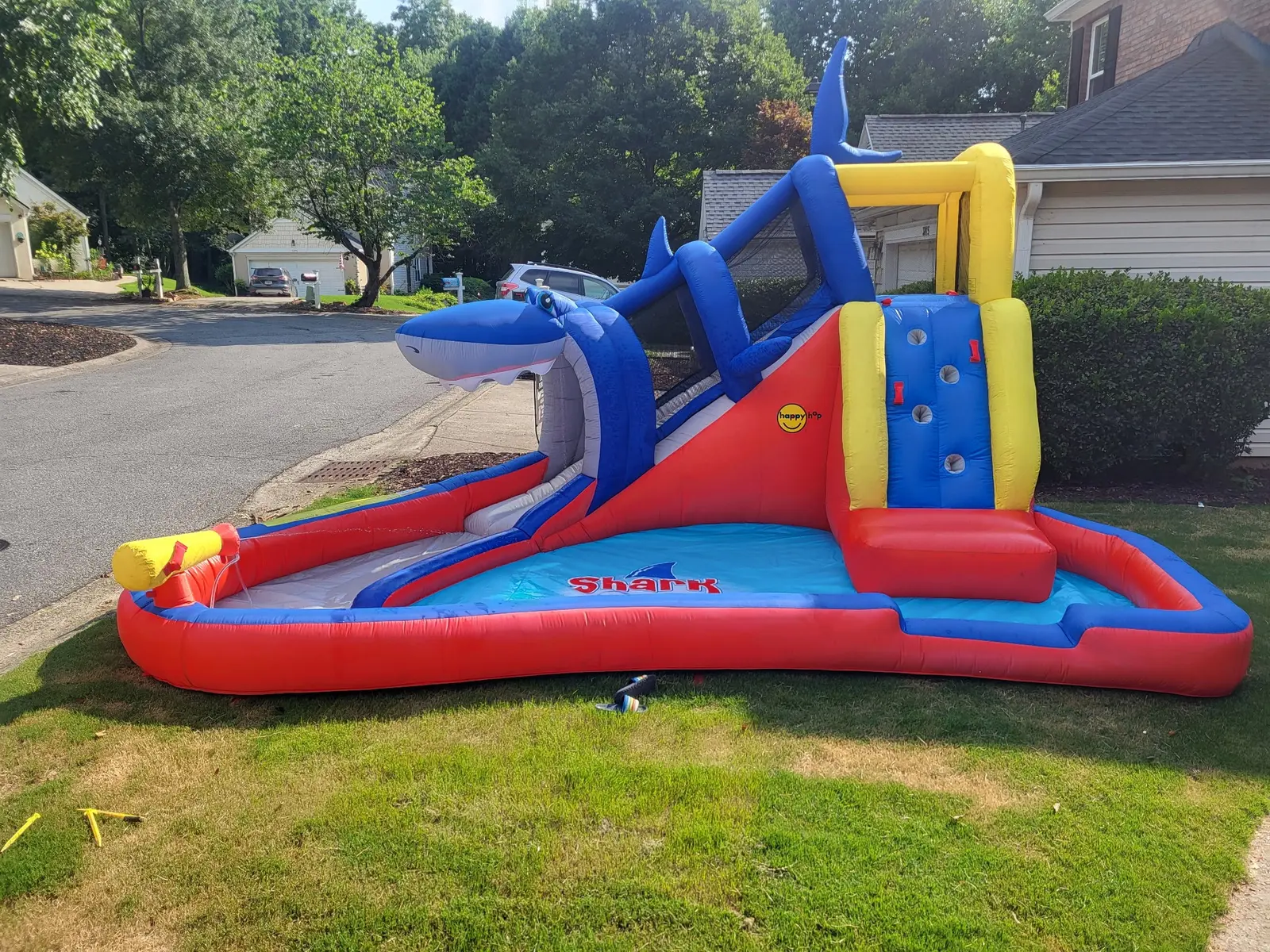 Red, yellow, and blue shark-themed toddler bounce house and slide set up outdoors